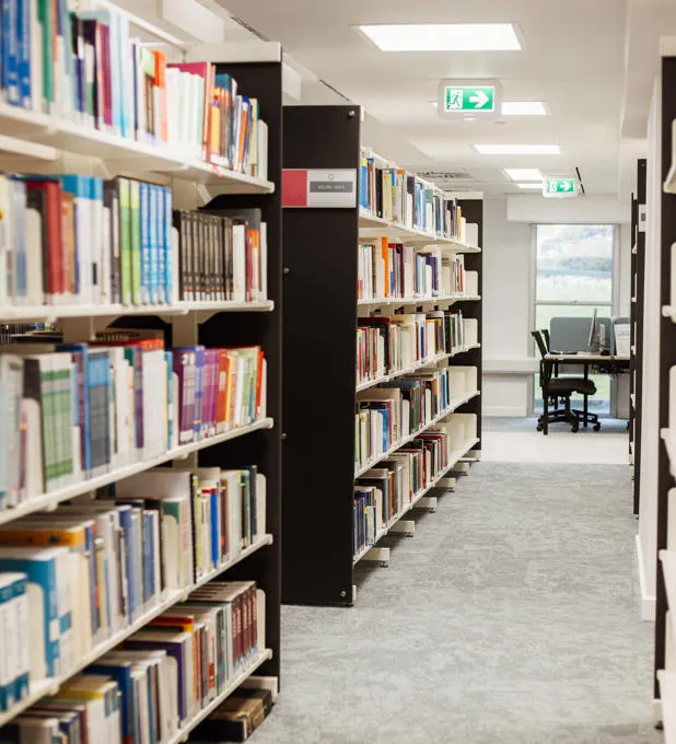 Rows of books with study spaces in the background.