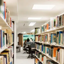 Rows of books on shelves with students studying in the background.