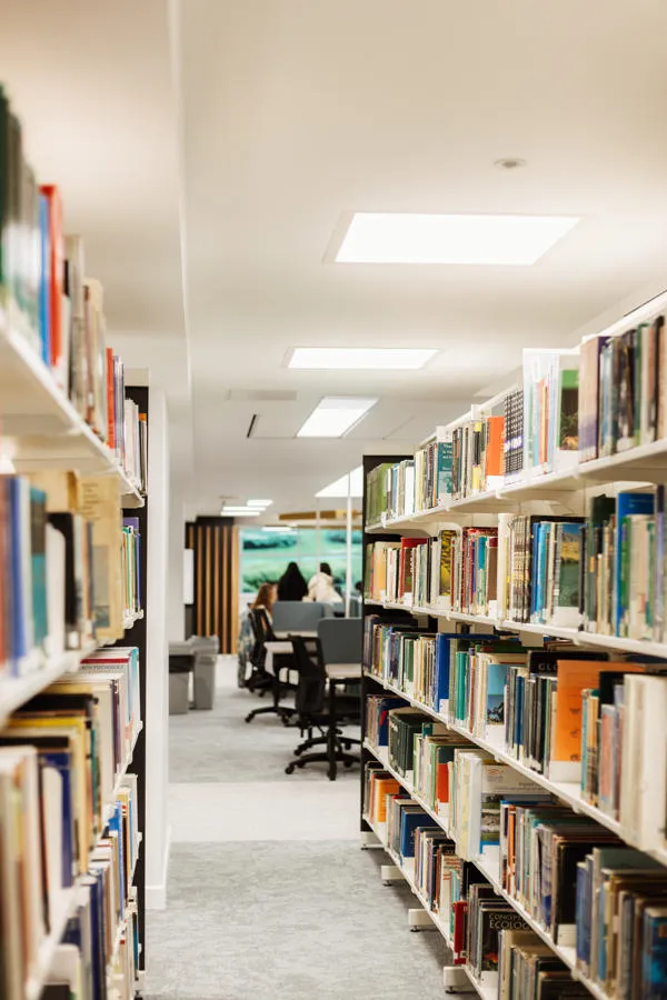 Rows of books on shelves with students studying in the background.