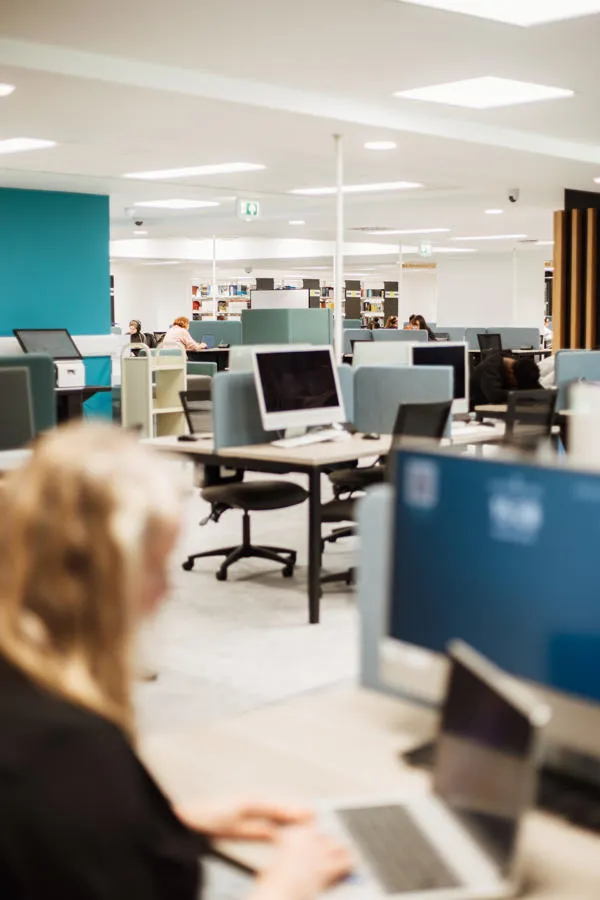 View of PCs with student in foreground working on a laptop.